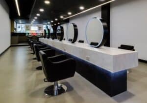 salon with mirrors chairs and white solid surfaces that gives a modern luxury finish