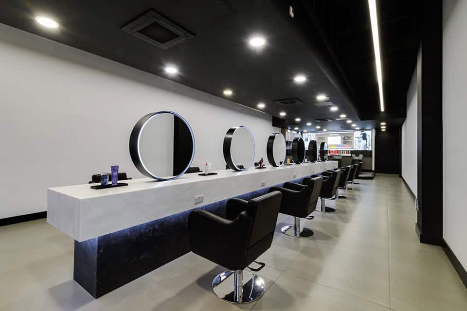 salon with mirrors chairs and white solid surfaces that gives a modern luxury finish